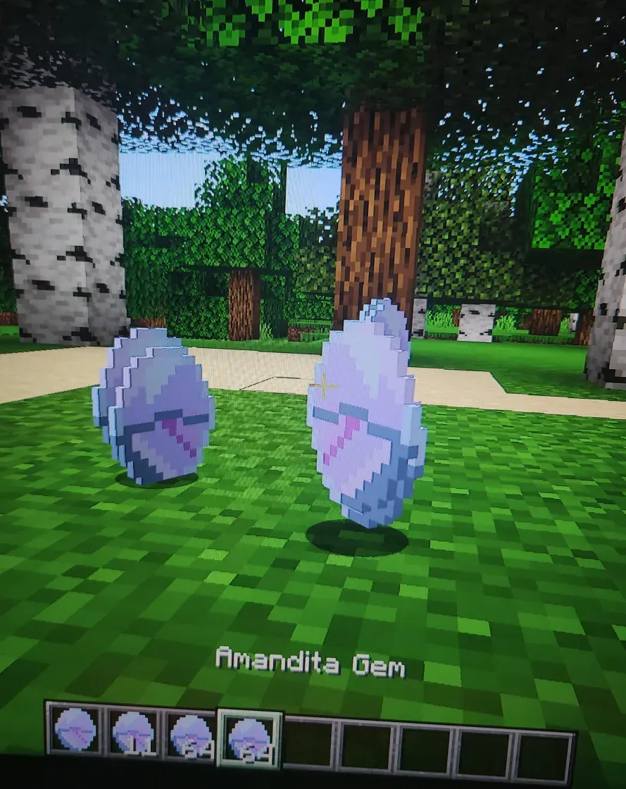 The Amandita Gem in the game: two of them dropped on the grass in a birch forest, pale lilac with a pink streak, above a hotbar holding four stacks of the gem.