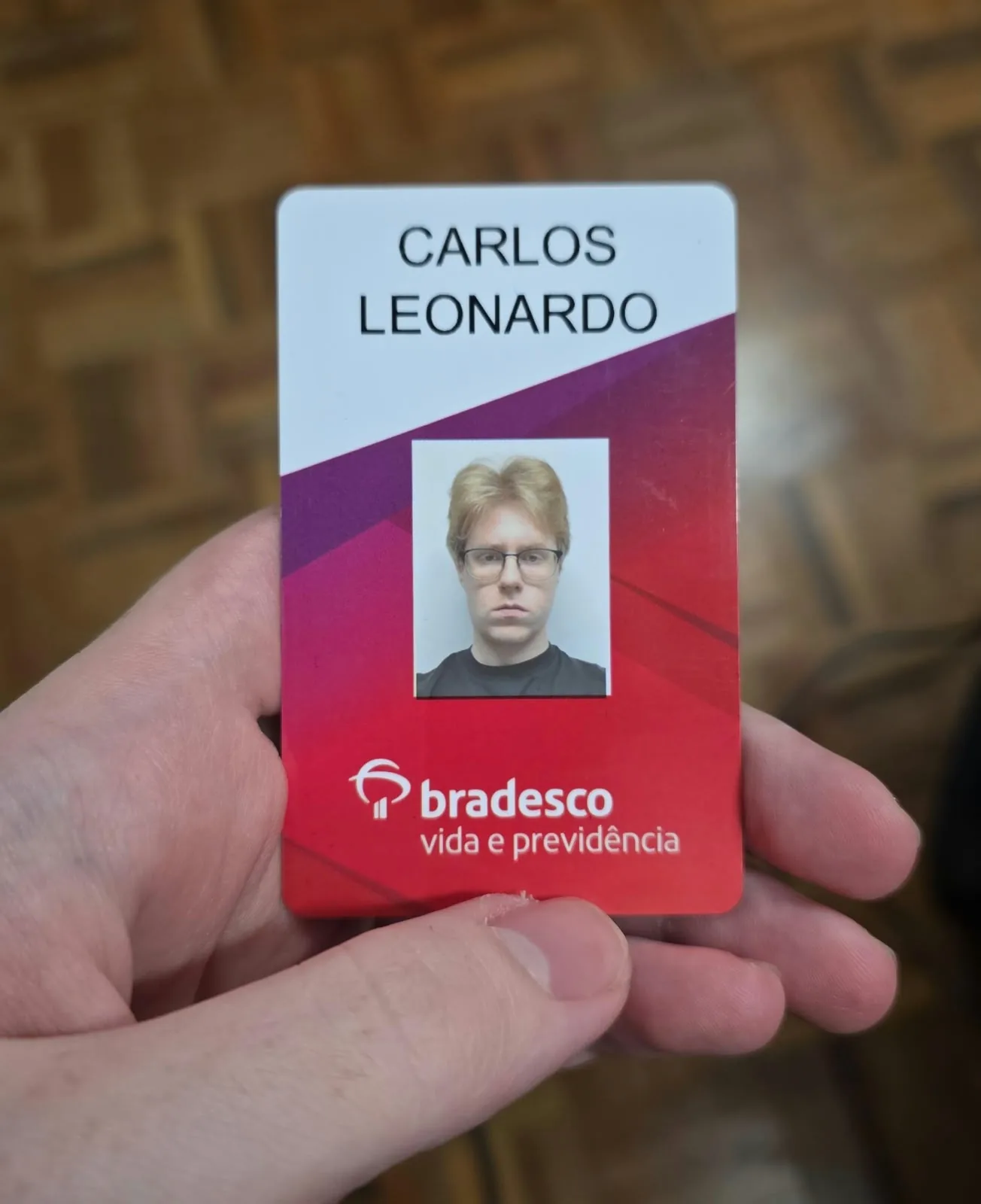 A hand holding a Bradesco Vida e Previdência badge issued to Carlos Leonardo.